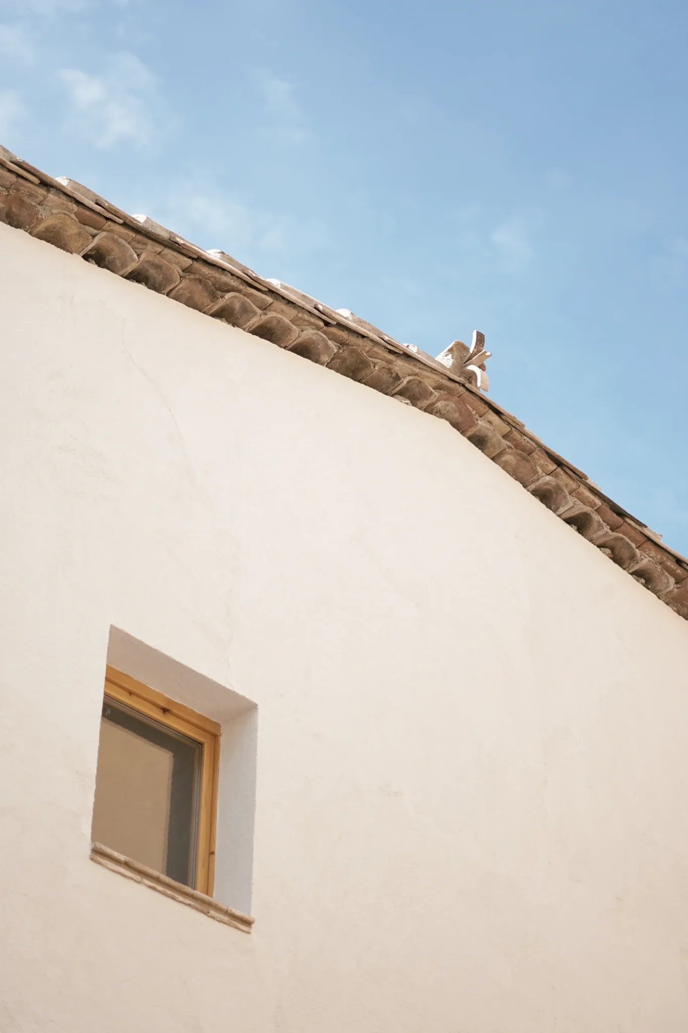 Alero de teja cerámica y ventana de madera en la fachada blanca de la reforma en Sant Llorenç Savall