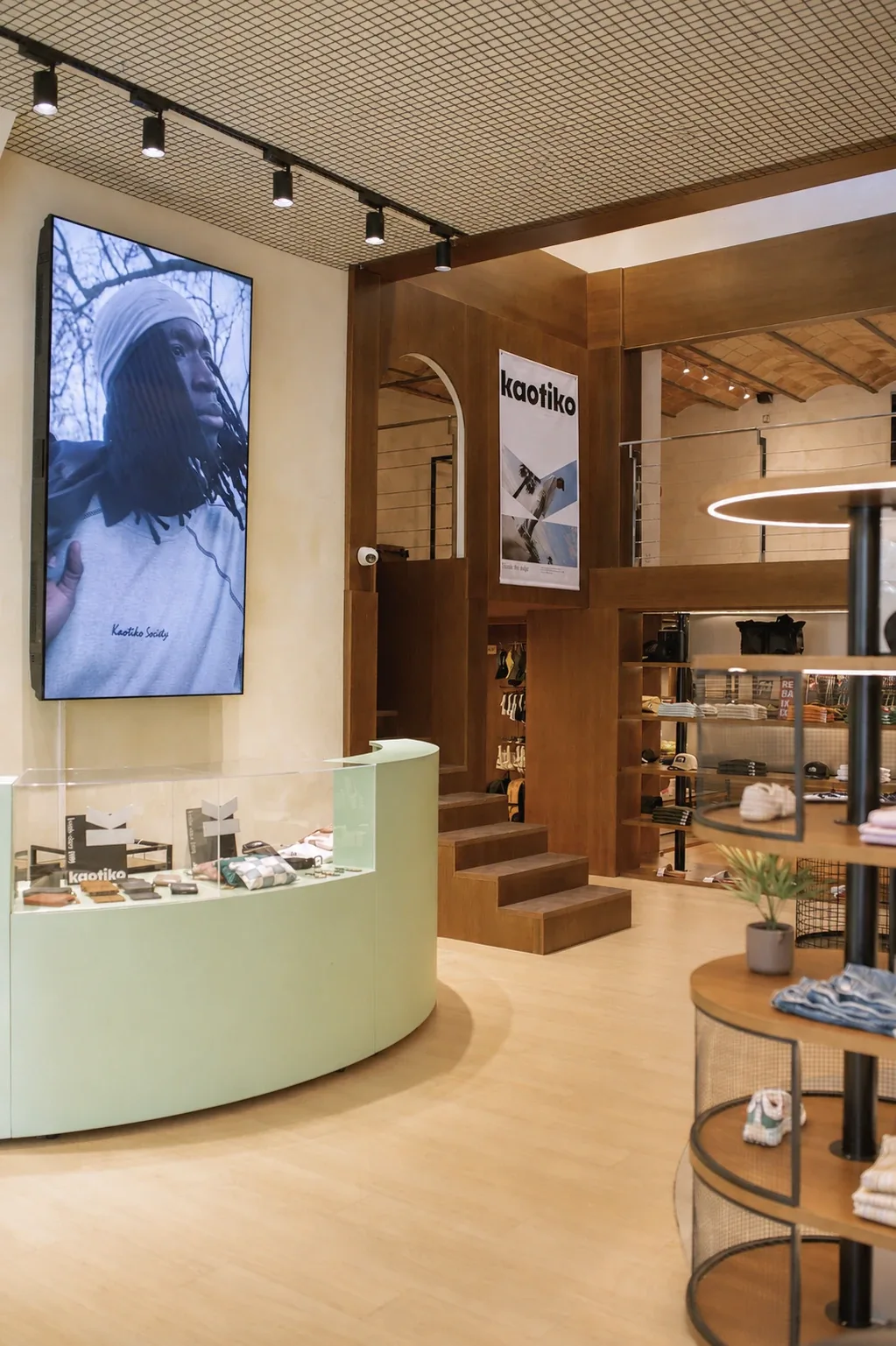 Pantalla audiovisual junto al mostrador y la escalera, diseño de espacio comercial Kaotiko, Manresa