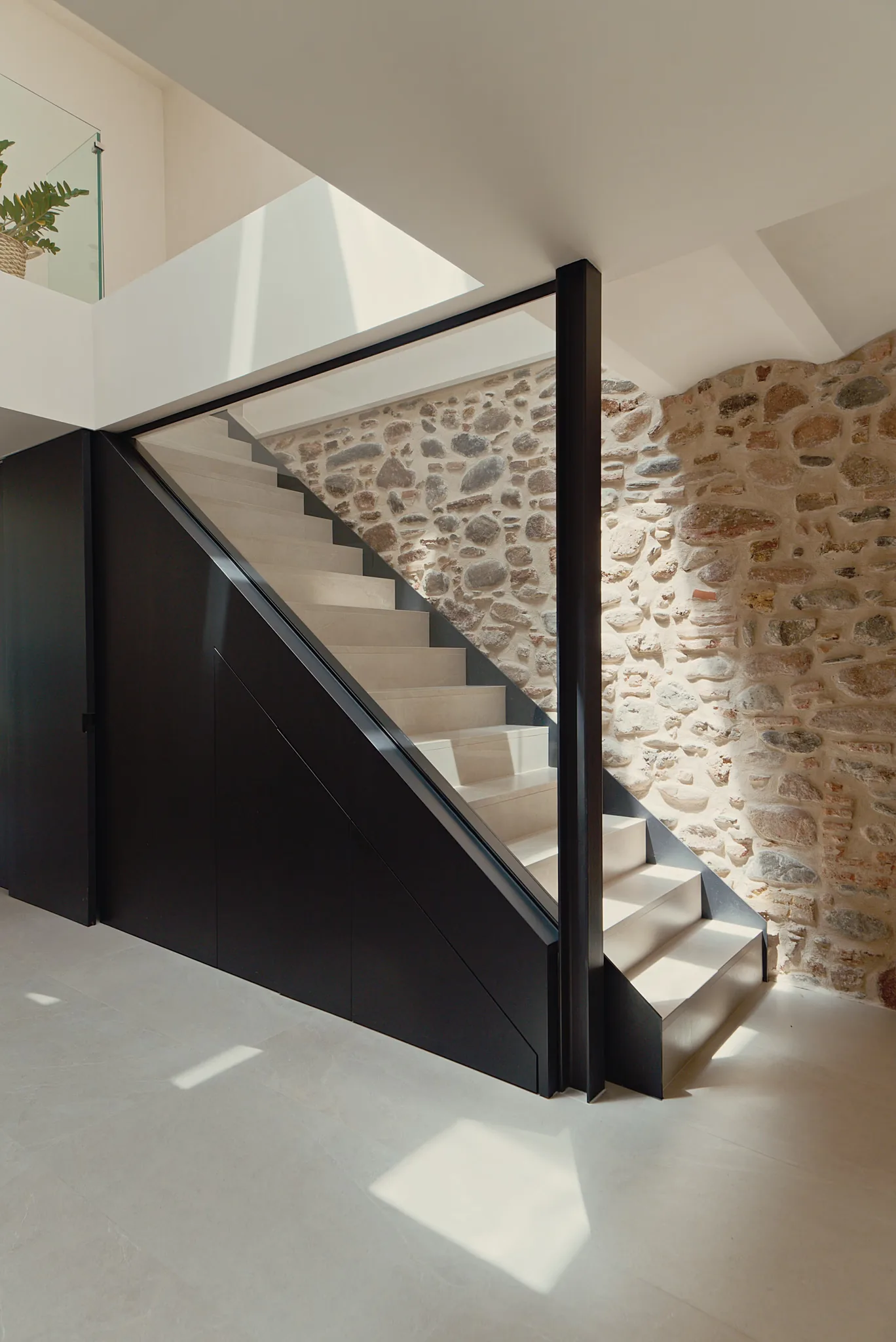 Escalera de acero y vidrio junto al muro de piedra original, reforma integral en Granollers, Barcelona